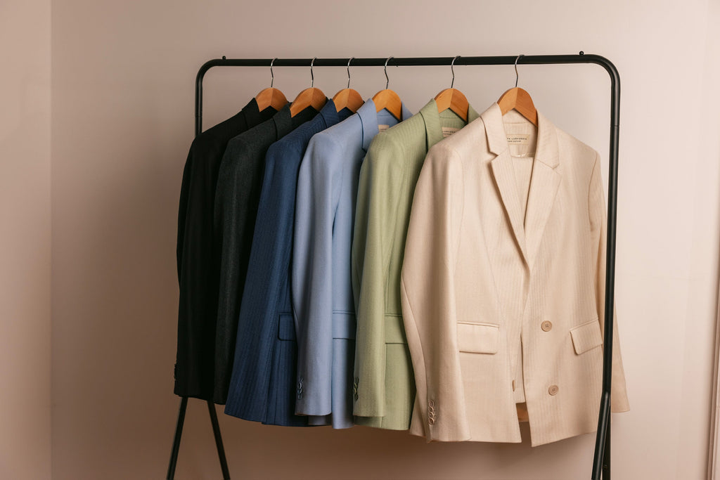 Six blazers hang side to side against a creme background.