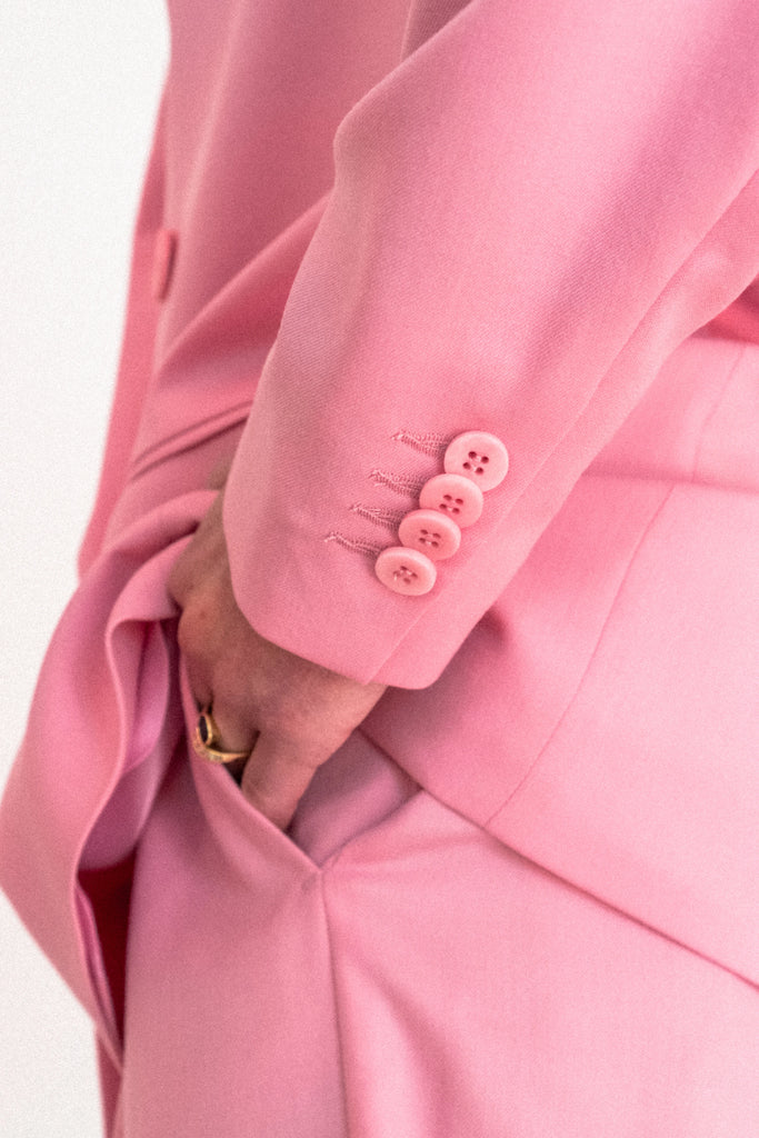 Close-up of a person wearing the ALVA Blazer in Candy Pink, with their hand in the pocket. The blazer sleeve features four matching pink buttons and intricate stitching details near the cuff. The person is also wearing a gold ring on their ring finger.