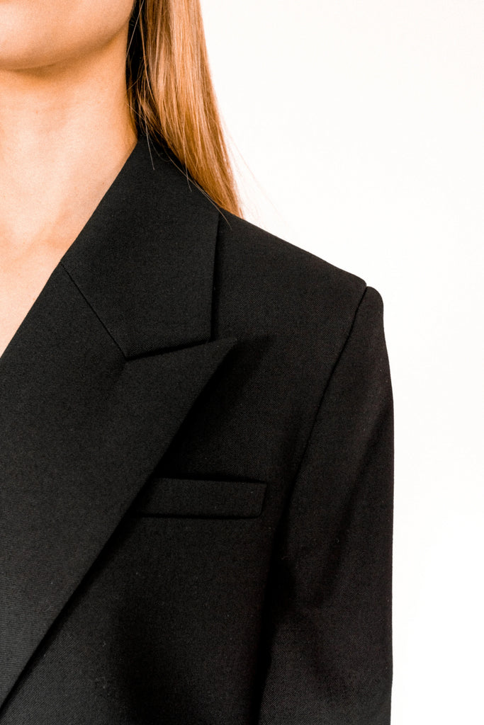 Close-up of a person wearing the ALVA Blazer in Tuxedo Black. Only the shoulder, lapel, and part of the chest and collar are visible.