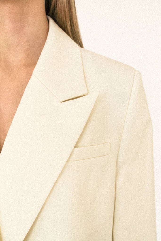Close-up of a person wearing the ALVA Blazer in Vanilla Creme. Only the shoulder, lapel, and part of the chest and collar are visible.