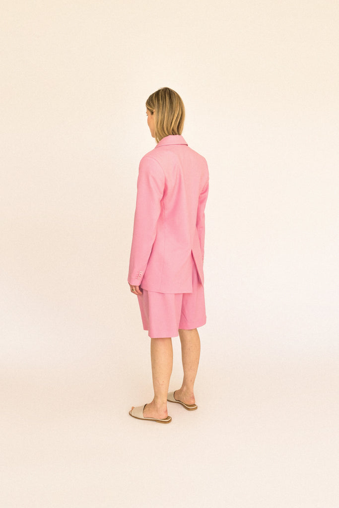 A person stands against a plain backdrop wearing the ALVA Blazer in Candy Pink, paired with matching knee-length shorts.
