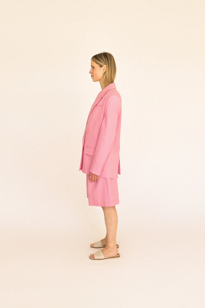 A person stands against a plain backdrop wearing the ALVA Blazer in Candy Pink, paired with matching knee-length shorts.
